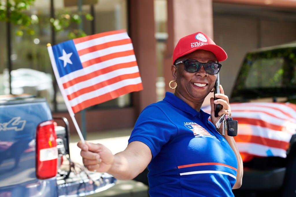 Woman in a blue LCACNJMA shirt waving a Liberian flag at the July 2023 Independence Day celebration in Trenton